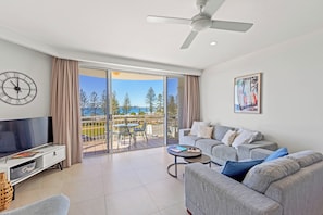 Relax in this stylish living room with a large flat-screen TV, comfortable sofa, and sliding glass door leading to a scenic outdoor area.