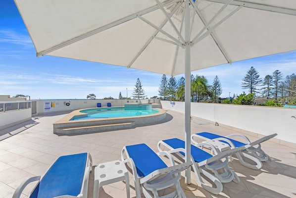 Relax by the rooftop pool, surrounded by a deck and lounge chairs under a shaded area.