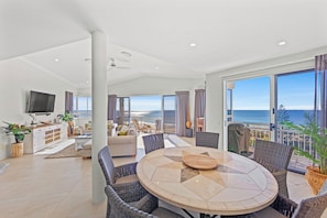 Enjoy a scenic ocean view from the comfort of this spacious living room, featuring a large dining table and comfortable seating.