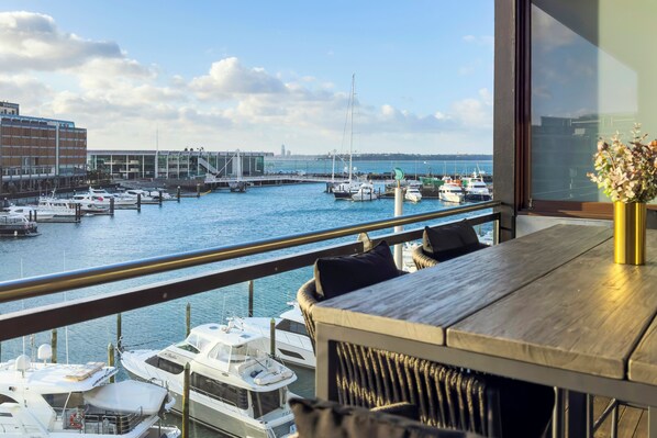 Enjoy the serene view of the marina from this balcony with a table and comfortable seating.