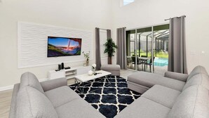 Ein modernes Wohnzimmer mit Flachbildfernseher, grauen Sofas, einem Couchtisch und einem gemusterten Teppich.