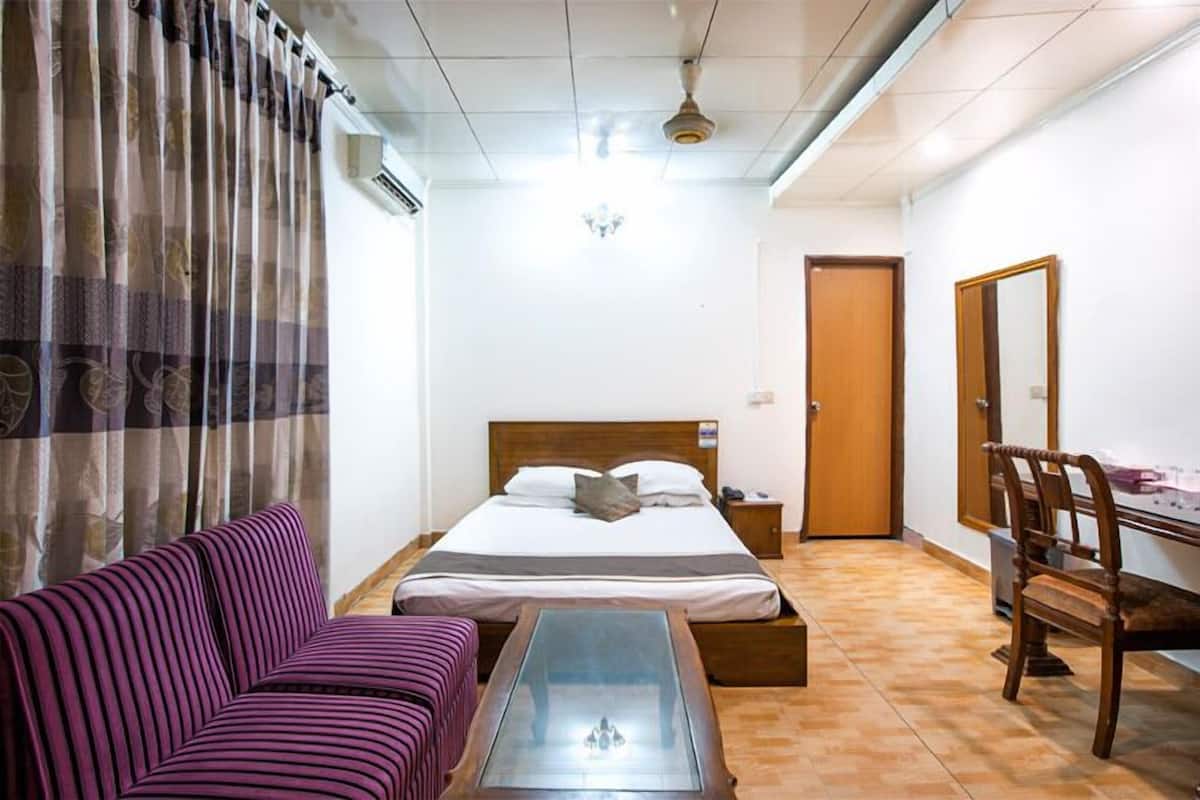 A bedroom with a bed, a purple sofa, a wooden chair, a small table, and a mirror.