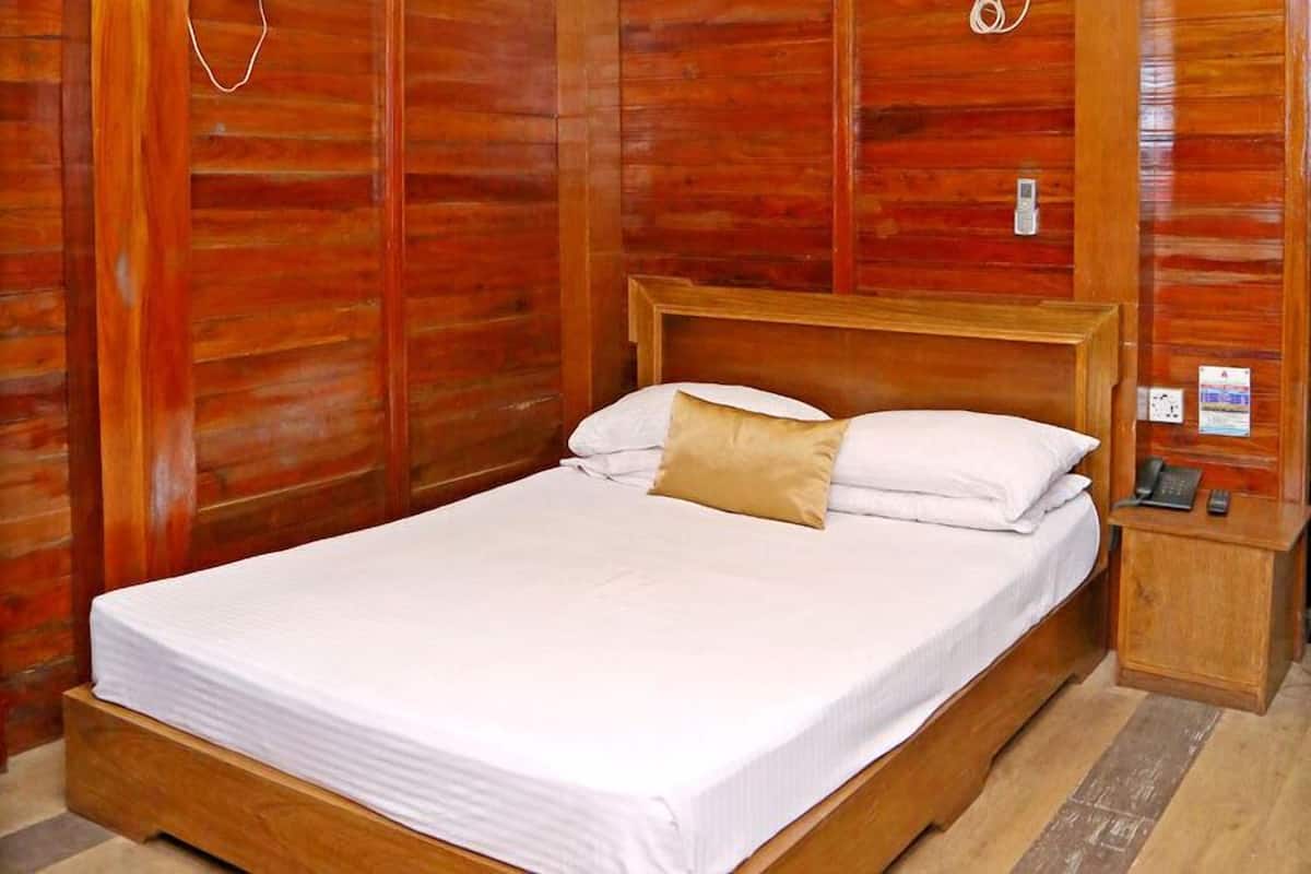 A wooden-framed bed with white bedding and a single tan pillow in a room with wooden paneling.