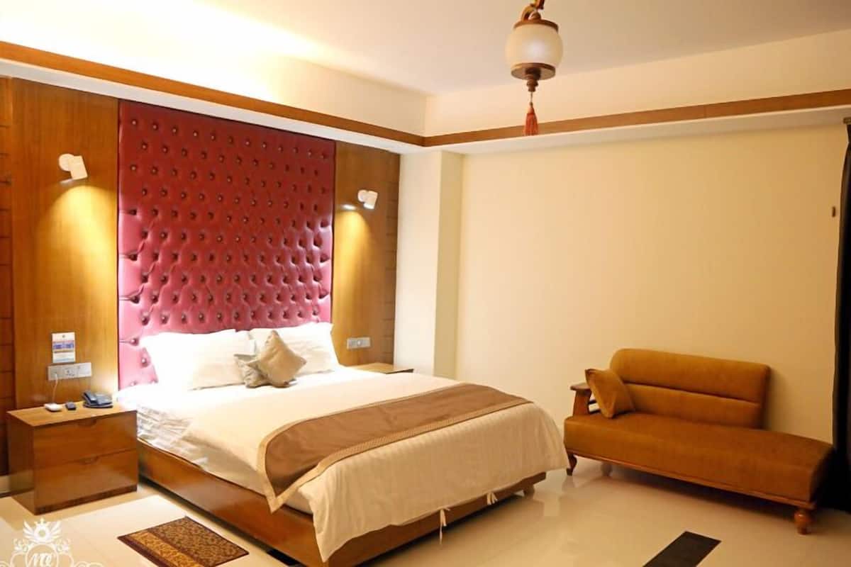 A bedroom with a large bed, a sofa, wooden nightstands, and a red tufted headboard.