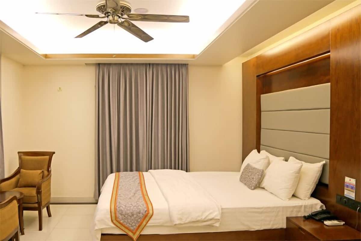 A hotel room with a bed, a wooden nightstand, a chair, a ceiling fan, and a window with curtains.