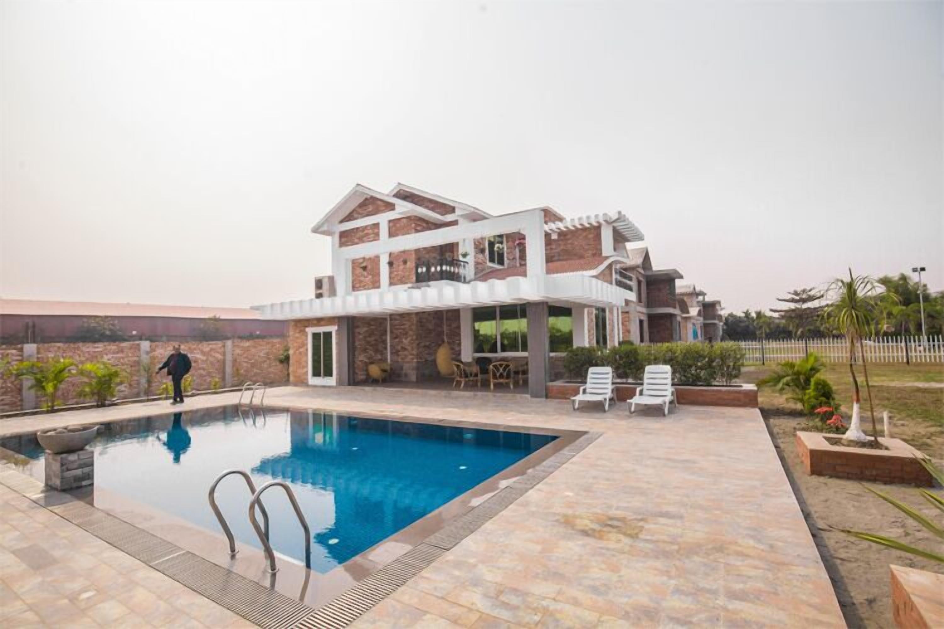 Una casa de dos pisos con piscina, mobiliario exterior y un jardín ajardinado.