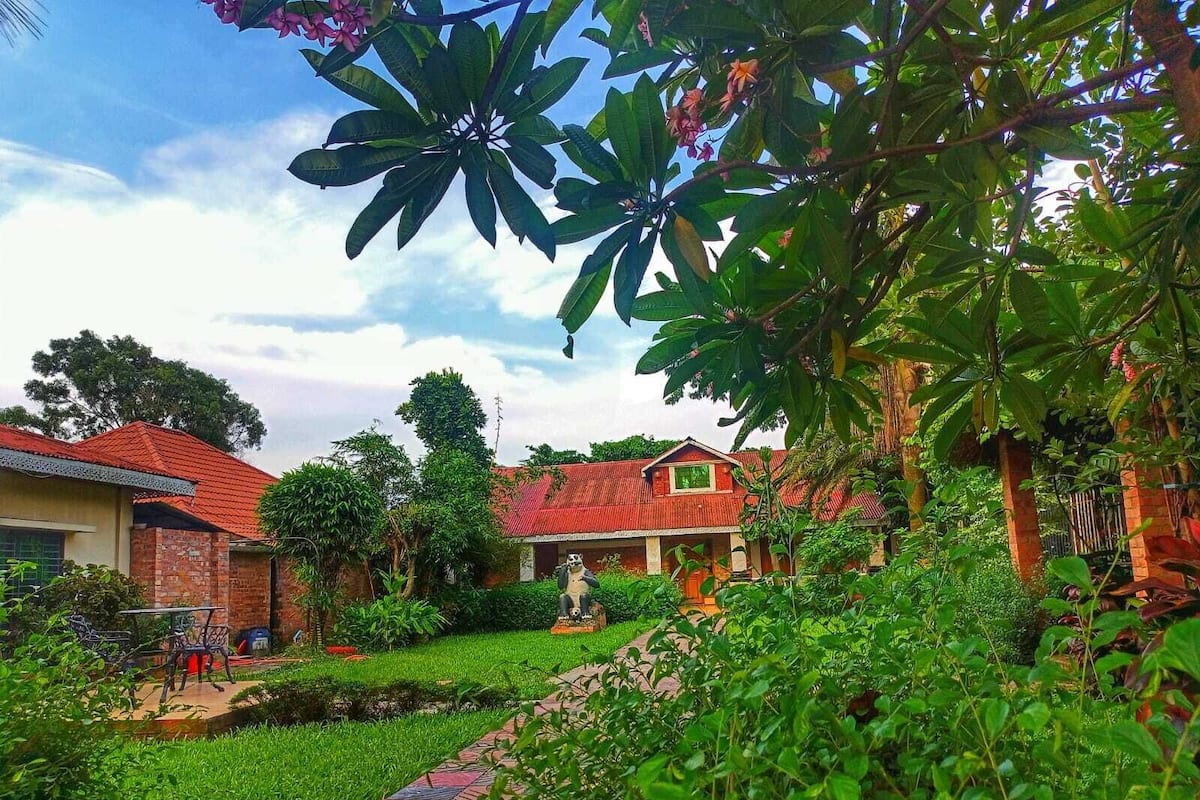 A residential area with a house featuring a red roof, a brick exterior, and a small garden with a paved pathway.