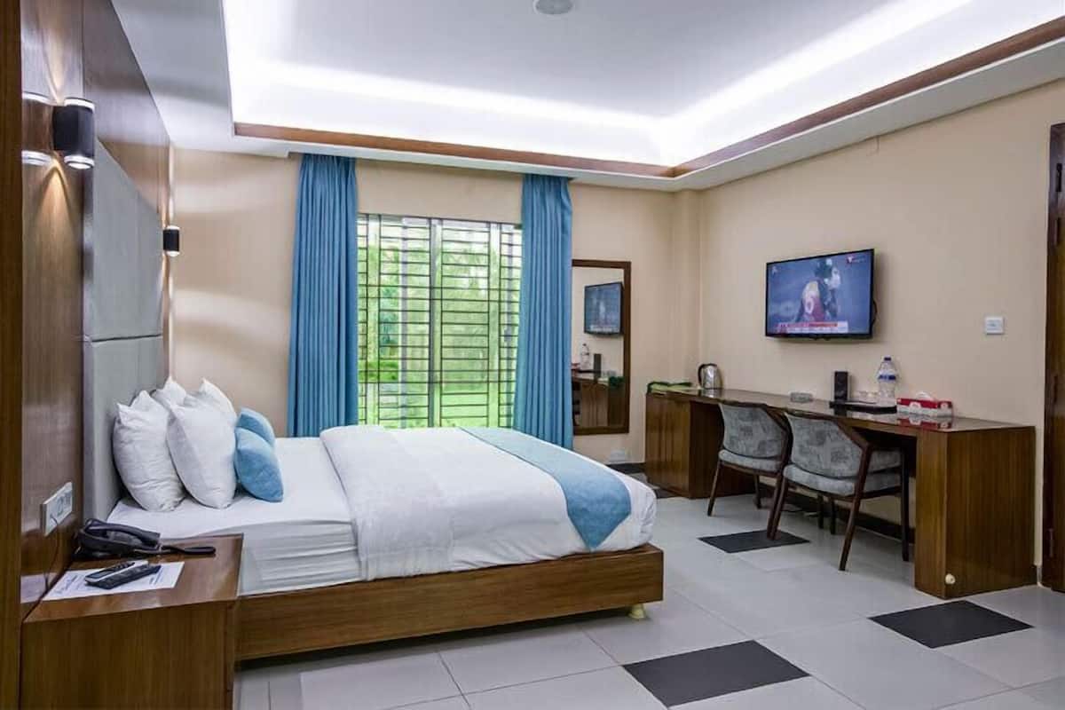 A hotel room with a bed, desk, TV, and a window with curtains.