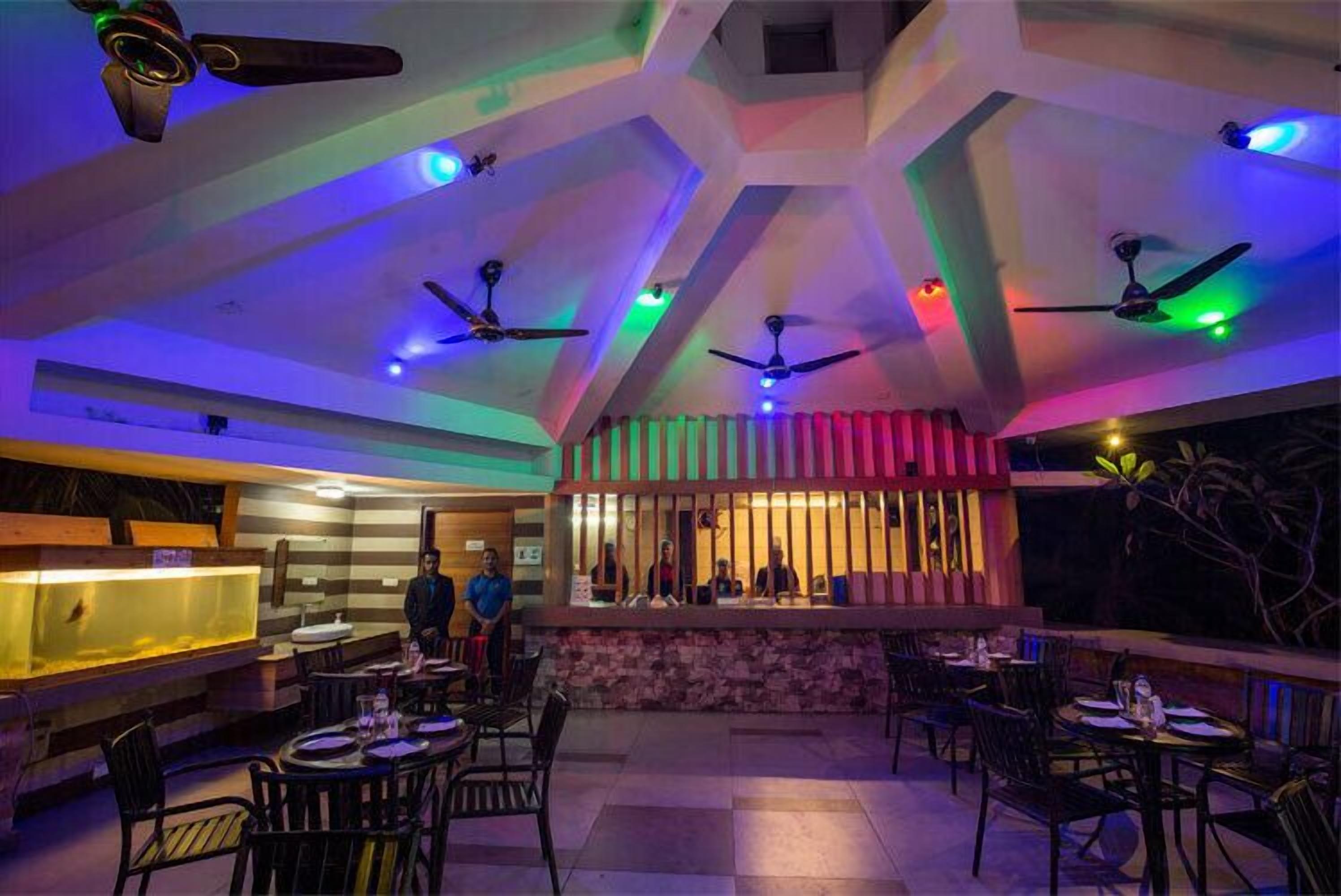 An indoor dining area with multiple tables and chairs, ceiling fans, and a counter with staff.