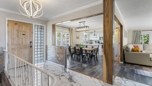 A spacious living area with a marble floor, a wooden door, and a dining area with a chandelier. - The Hill House Mtn Views Hot Tub Fire Pit & BBQs (Reno)
