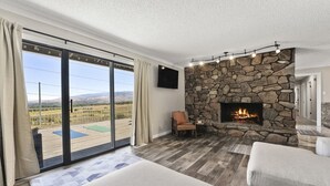 A room with a stone fireplace, a large sliding glass door to a deck, and a flat-screen TV mounted on the wall. - The Hill House Mtn Views Hot Tub Fire Pit & BBQs (Reno)
