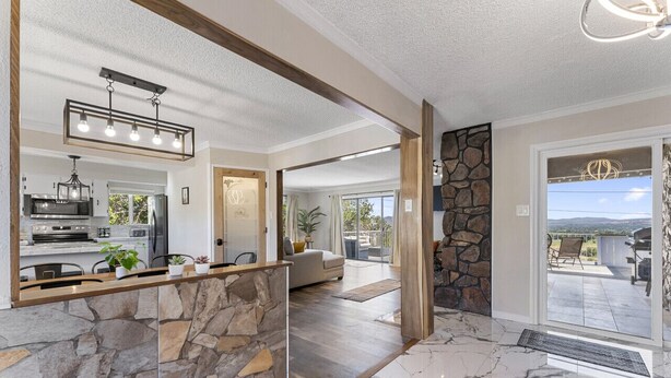 A spacious living area with a stone accent wall, a kitchen with modern appliances, and a patio with a view. - The Hill House Mtn Views Hot Tub Fire Pit & BBQs (Reno)