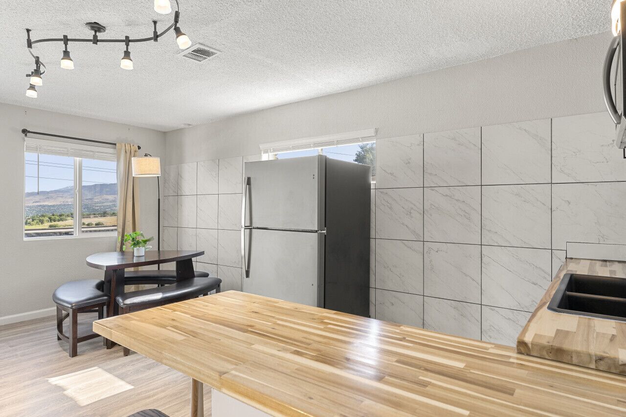 Una cocina moderna con protector mural de mármol, refrigerador empotrado, encimera de madera y un comedor con banco y mesa.