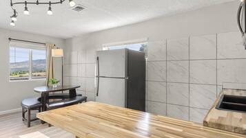 Una cocina moderna con protector mural de mármol, refrigerador empotrado, encimera de madera y un comedor con banco y mesa.