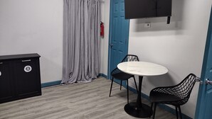 Une pièce avec une table ronde, deux chaises, un meuble noir, une porte bleue et un téléviseur fixé au mur.