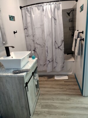 A bathroom with a white sink, a shower curtain, and a bathtub. - Luxury In A Quaint Little Package (Oshkosh)