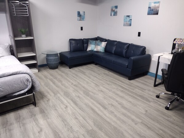 A modern bedroom with a bed, a dark blue sectional sofa, a small round table, and a desk with a chair. - Luxury In A Quaint Little Package (Oshkosh)