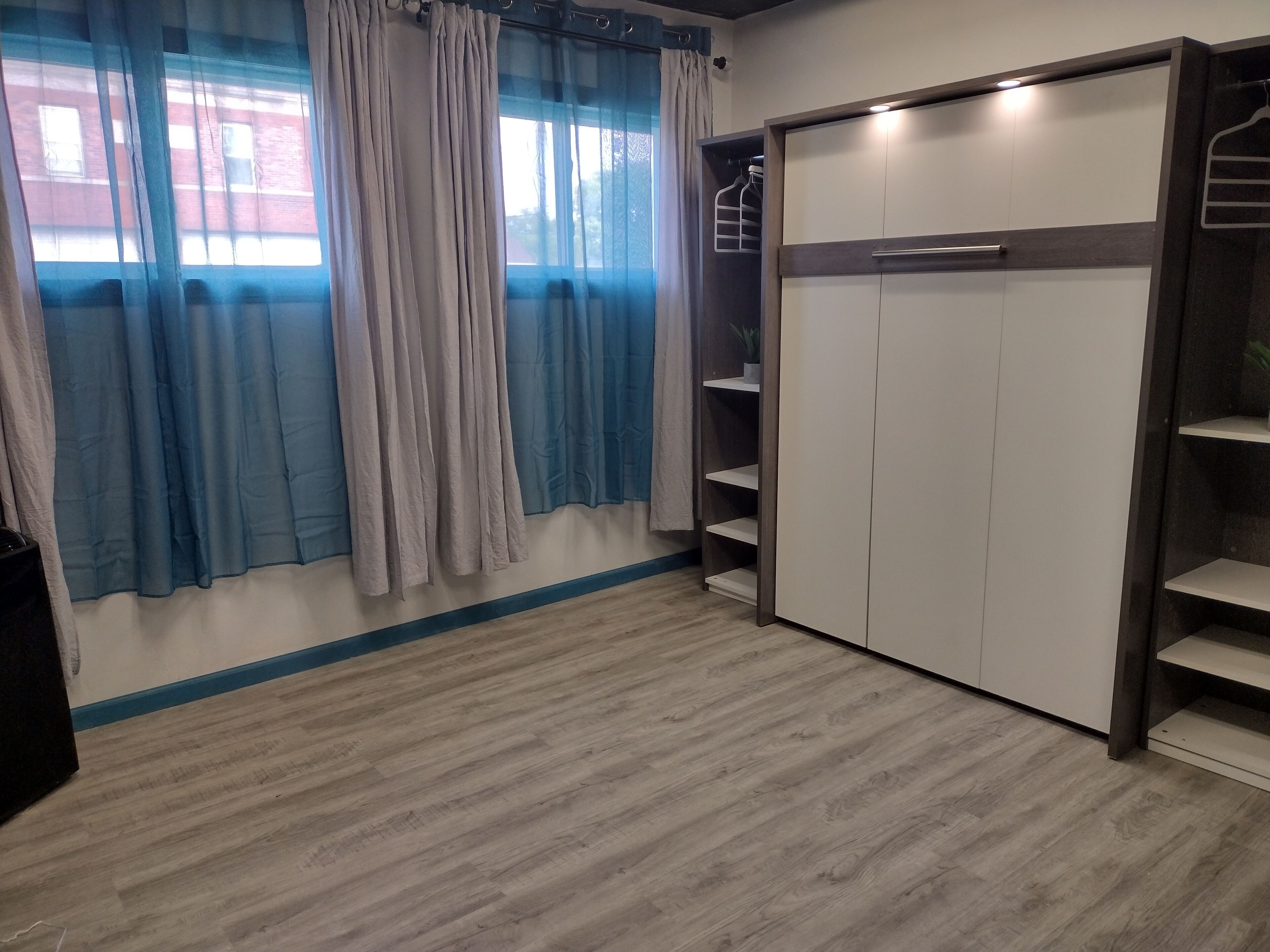 Ein Zimmer mit Kleiderschrank, Regalen und einem fenster mit Vorhängen.