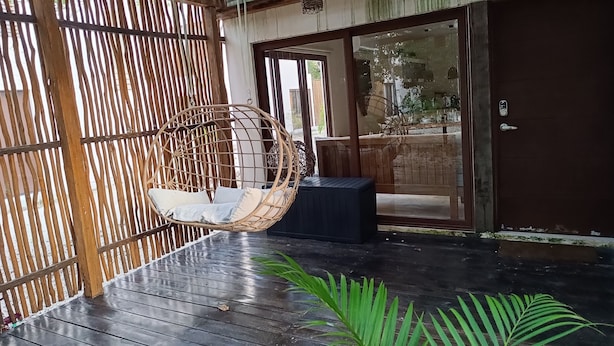 Une terrasse en bois avec un fauteuil suspendu, une porte vitrée et une plante en pot.