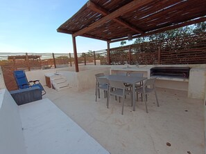 Une terrasse extérieure dotée d’une pergola, d’un barbecue et d’une table avec des chaises.