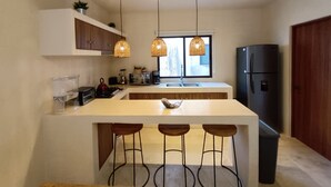 Une cuisine moderne dotée d’un îlot central, de luminaires suspendus, d’un réfrigérateur et d’une fenêtre offrant une vue agréable.