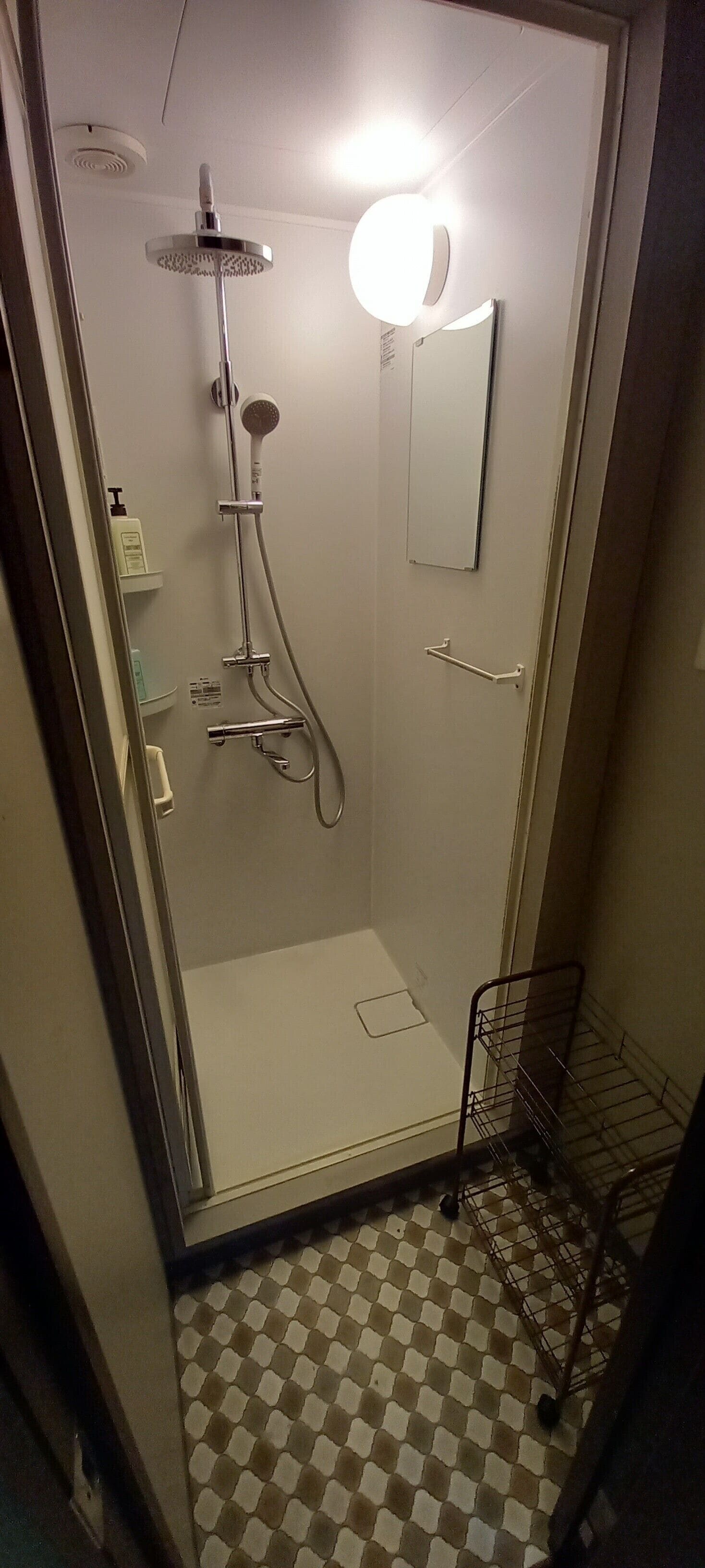 Un baño pequeño con azulejos, una ducha, un inodoro y un espejo.