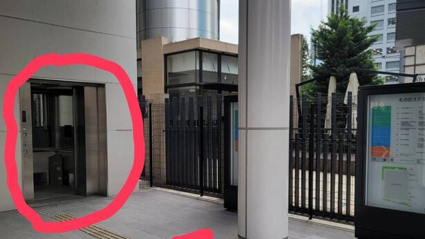 A modern building entrance with a glass door, a metal fence, and a digital information board.