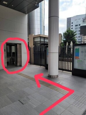 A modern building entrance with a glass door, a metal fence, and a digital information board. - Wasabi Mita Hotel (Tokyo)