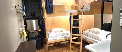 A compact room with bunk beds, a small kitchenette, and a wooden floor.