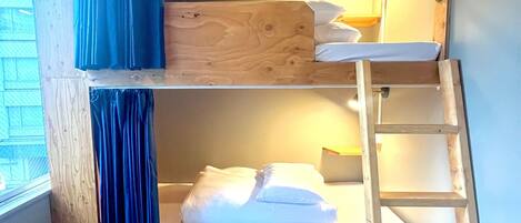A bunk bed with a wooden ladder, a window with blue curtains, and a wooden floor.