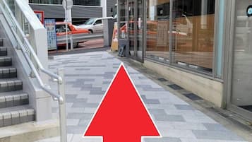 A modern building with a staircase leading to an entrance, a red arrow pointing upwards, and a glass facade.