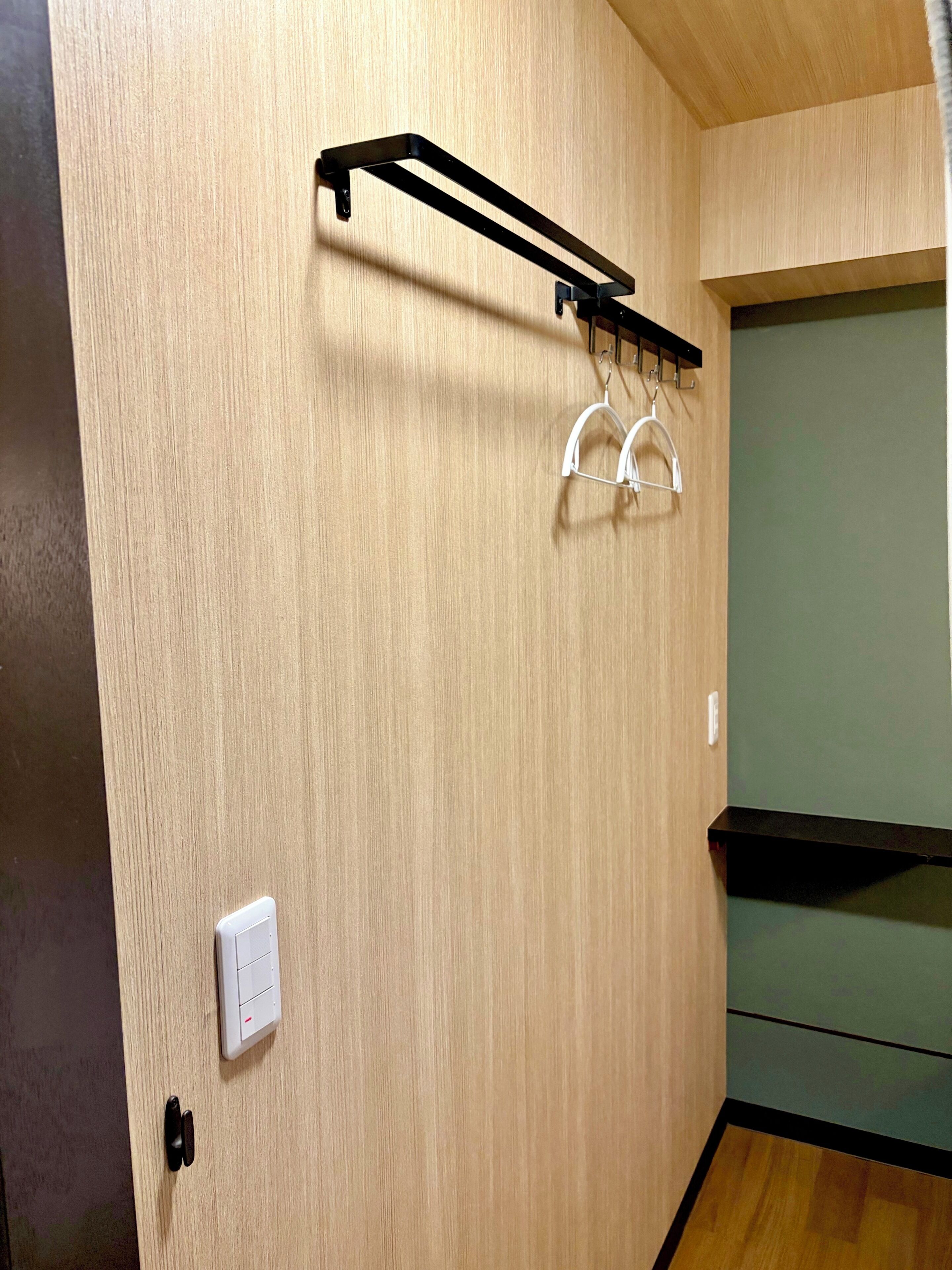 Une pièce avec un mur en bois, un portant en métal noir avec deux cintres blancs, un interrupteur blanc et une armoire verte.