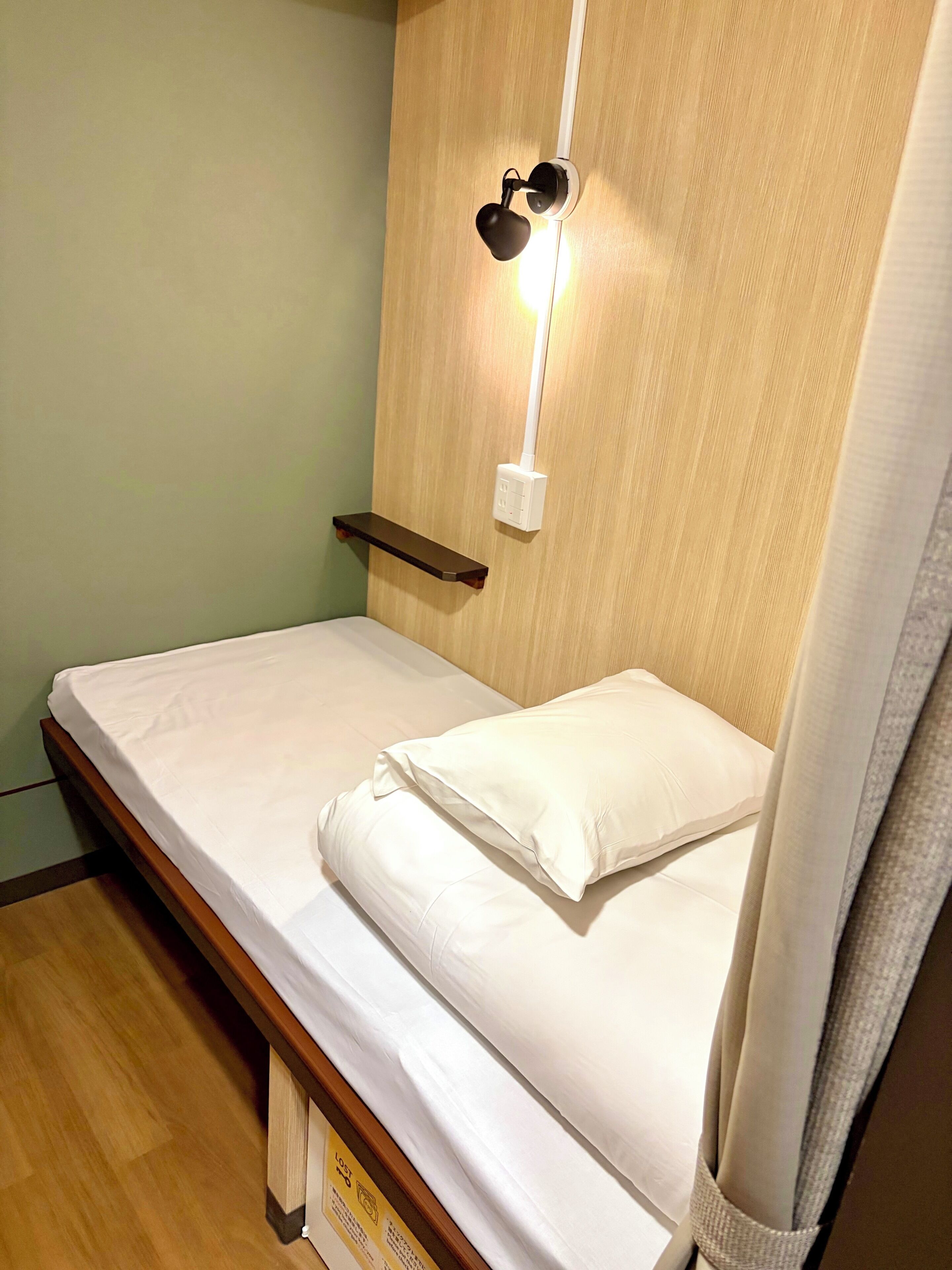 A single bed with a wooden headboard, a bedside table, and a wall-mounted light fixture.