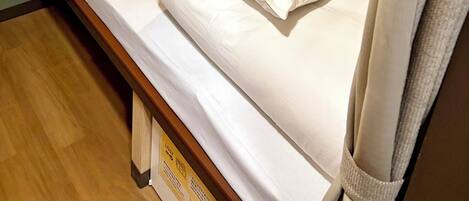 A single bed with a wooden headboard, a bedside table, and a wall-mounted light fixture.