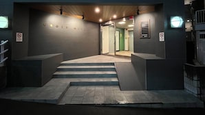 A modern building entrance with a staircase leading to an elevator. The name "CROSS MITA" is displayed on the wall.
