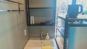 A compact bathroom with a white sink, a towel rack, and a shelf with toiletries.