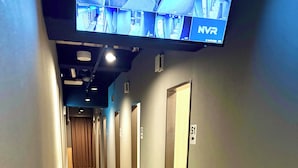A hallway with multiple doors, a television mounted on the wall, and a wooden floor.