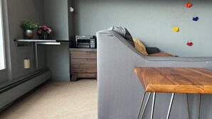 Een moderne woonkamer met een grijze bank, een houten salontafel, een printer en een kleine plant op een plank.