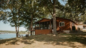 Une cabane en bois dotée de grandes fenêtres, d’une terrasse et offrant une vue sur un lac.