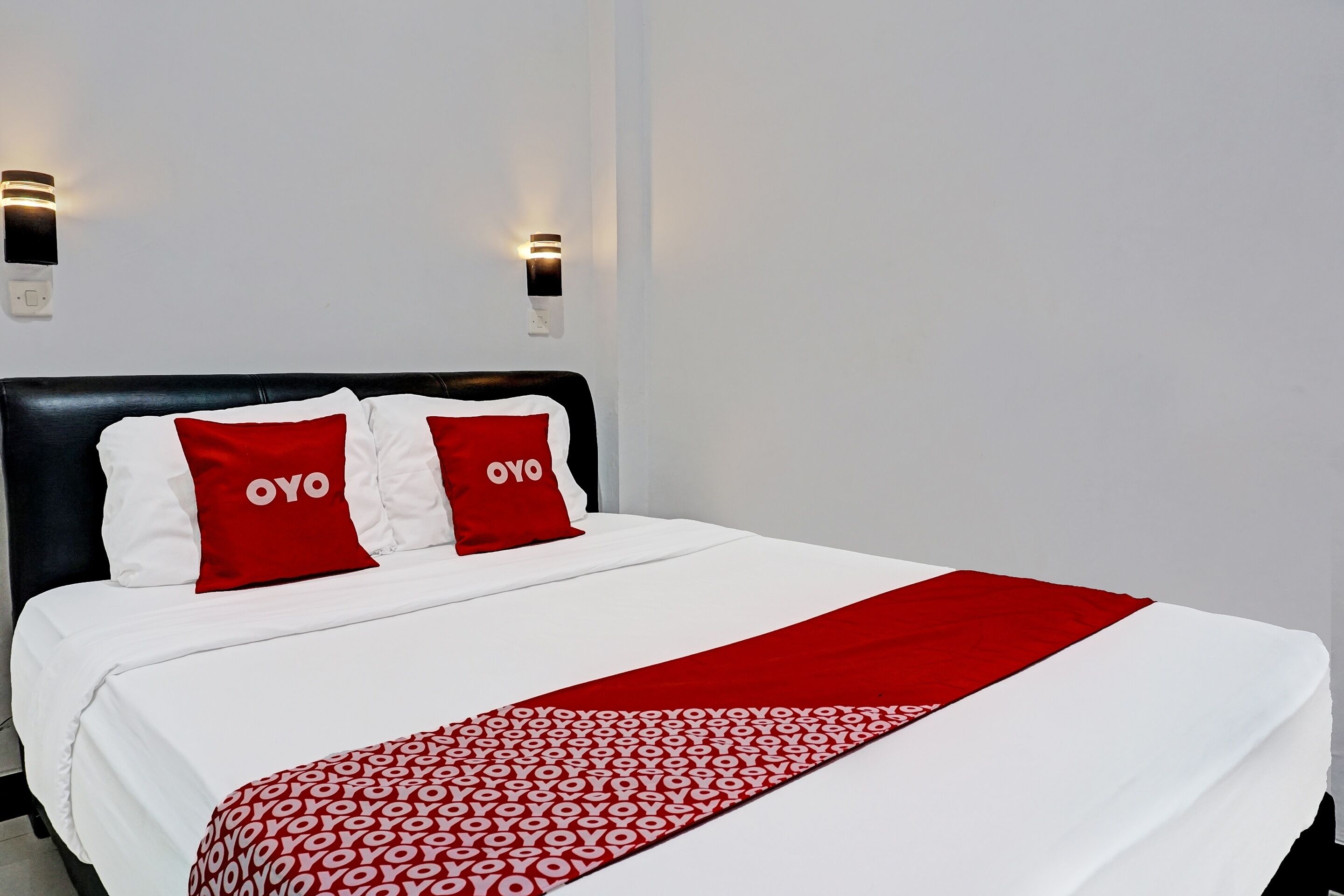 A hotel room with a black headboard, white bedding, and red accents including pillows and a throw blanket.