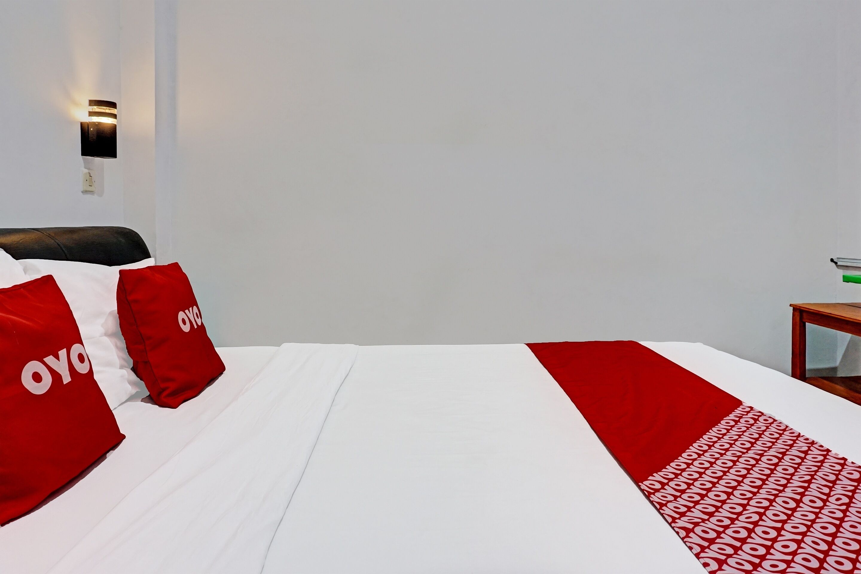A hotel room with a neatly made bed, a bedside table, and a wall-mounted light fixture.