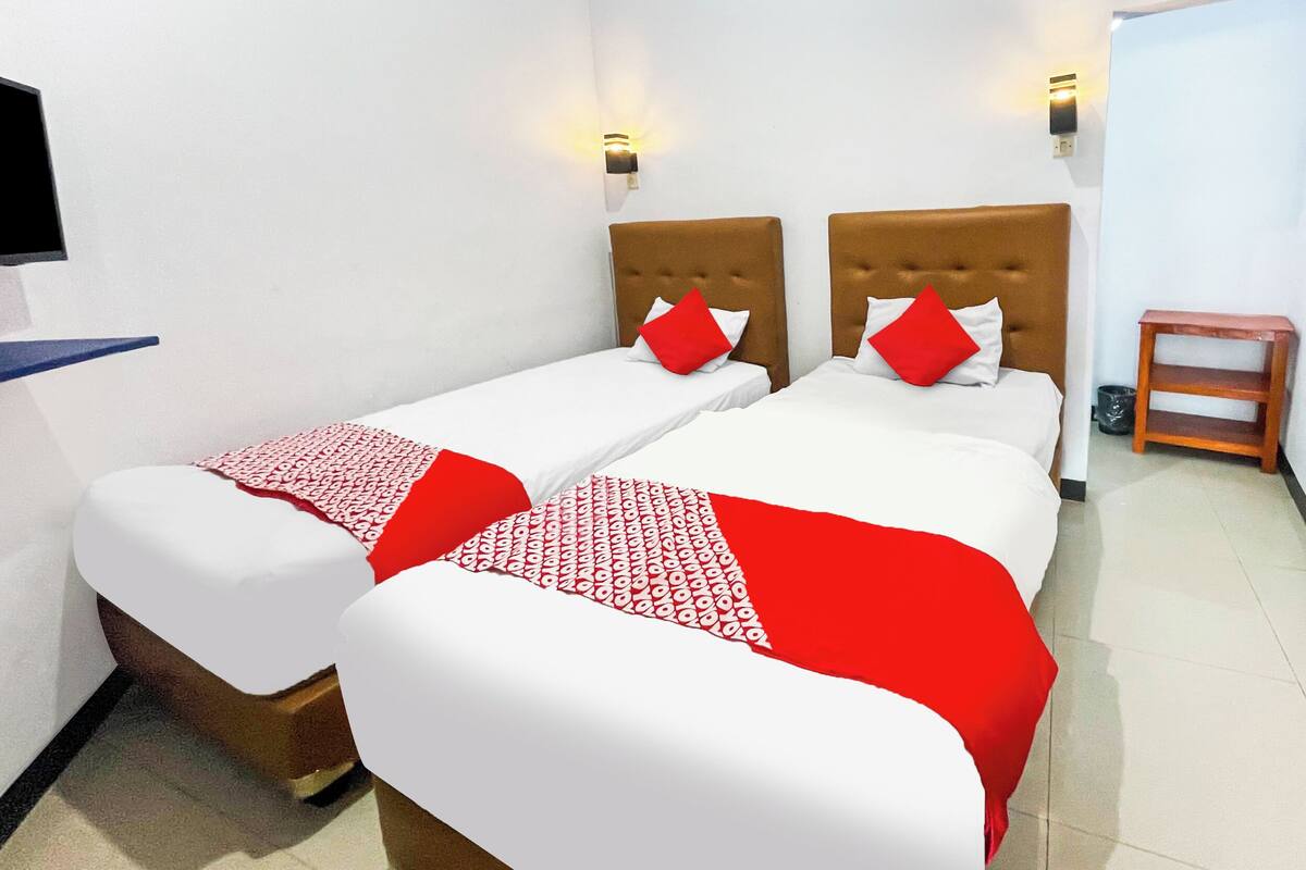 A hotel room with two beds, each with a headboard, a small wooden nightstand, and a wall-mounted TV.