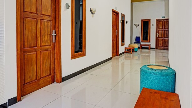 A hallway with wooden doors, a blue ottoman, and a small wooden table. - OYO 91599 Penginapan Mutiara Madiun (Jiwan)