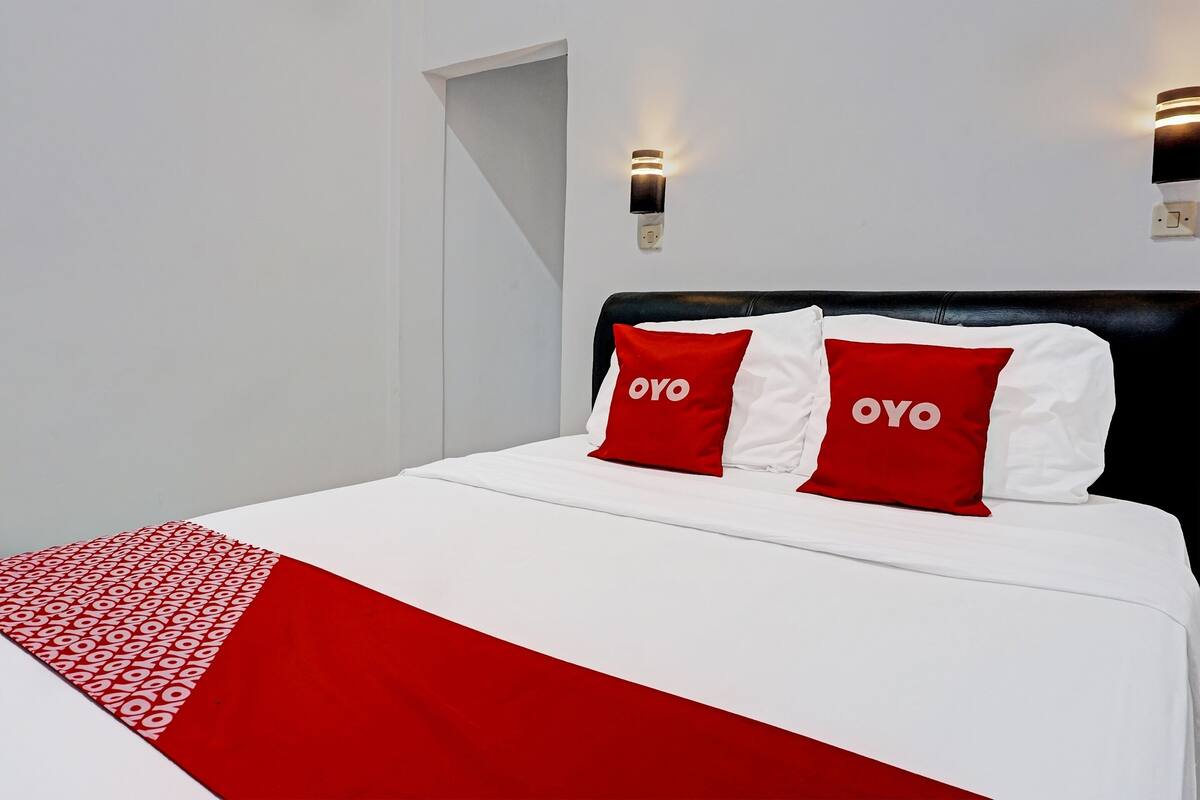 A bed with white bedding and two red pillows with the word "OYO" on them.