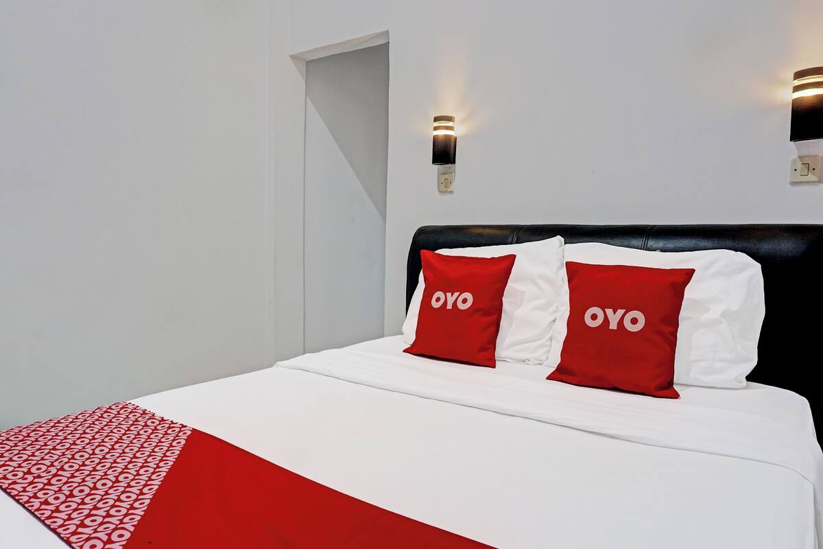 A bed with white bedding and two red pillows with 'OYO' text, a black headboard, and two wall-mounted lights.