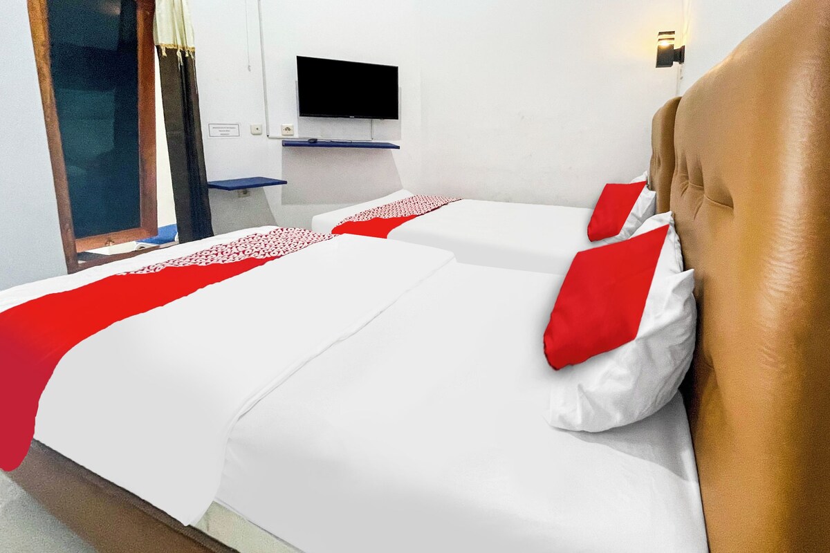 Habitació d'hotel amb dos llits, un televisor fixat a la paret i una finestra amb cortines.