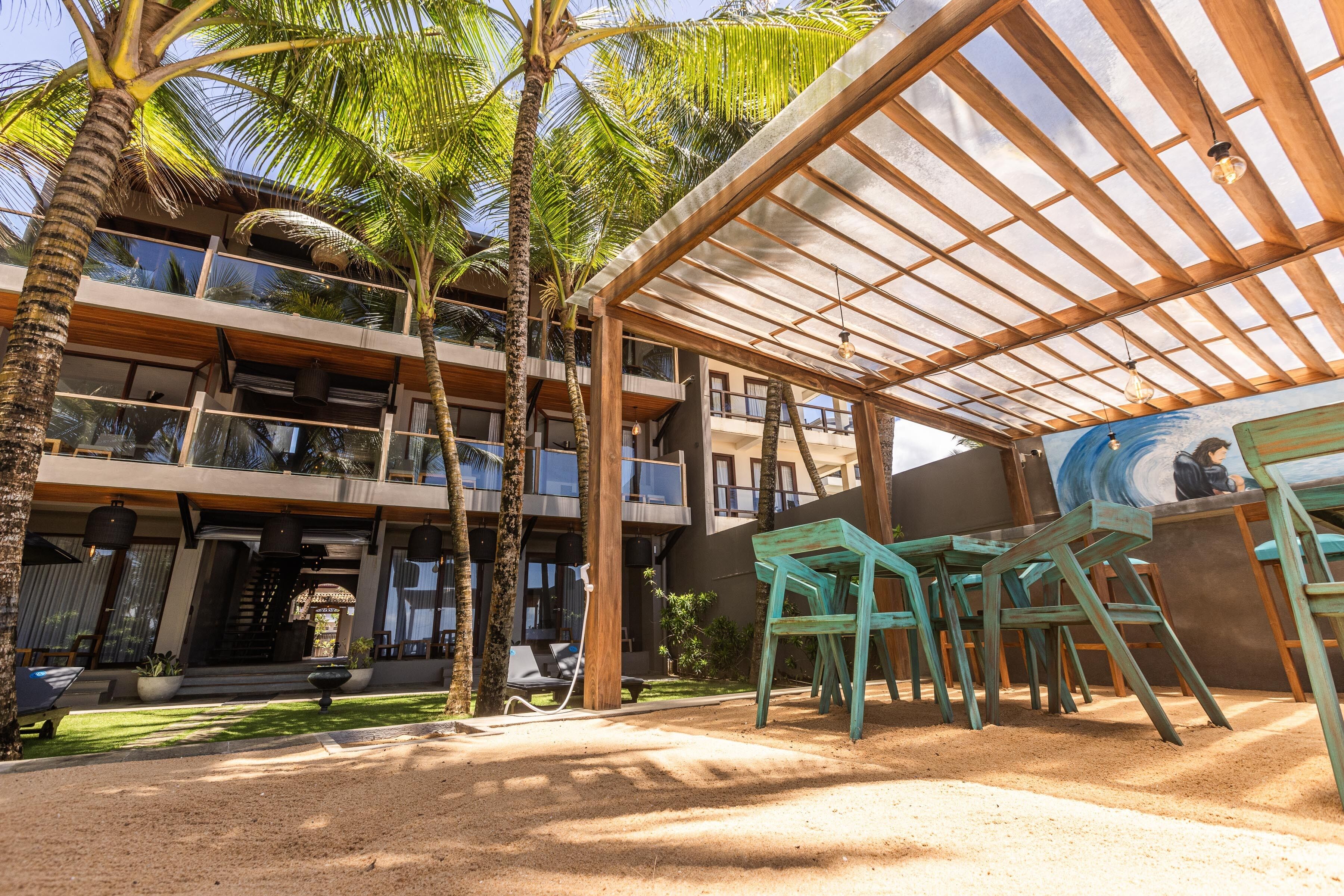 A modern building with multiple balconies, outdoor seating, and palm trees.
