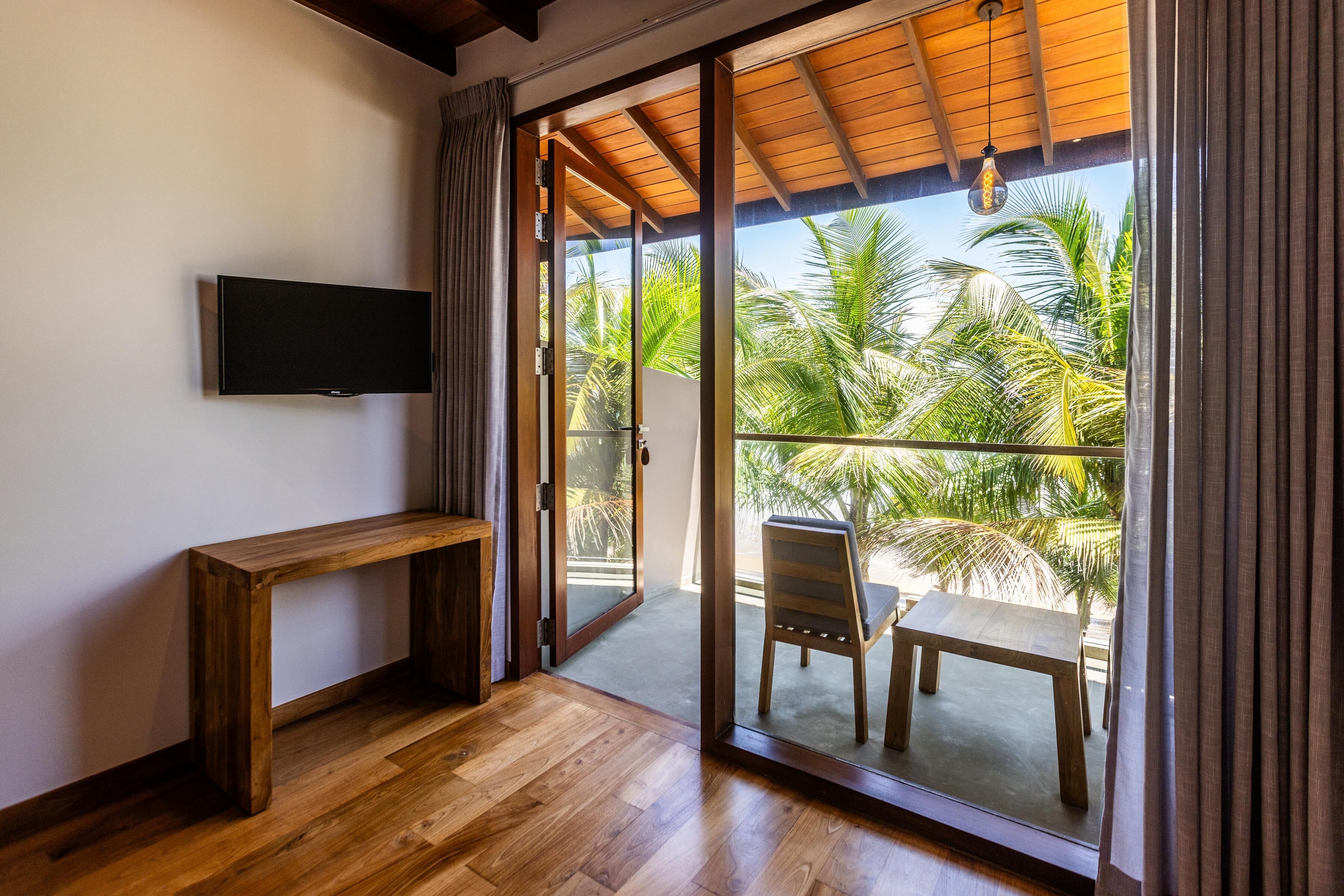 A room with a wooden bench, a flat-screen TV, and a sliding glass door leading to an outdoor area with a table and chairs.