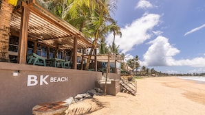 A beachfront property with a wooden structure, a sign reading "BK Beach Cafe," and a sandy beach.