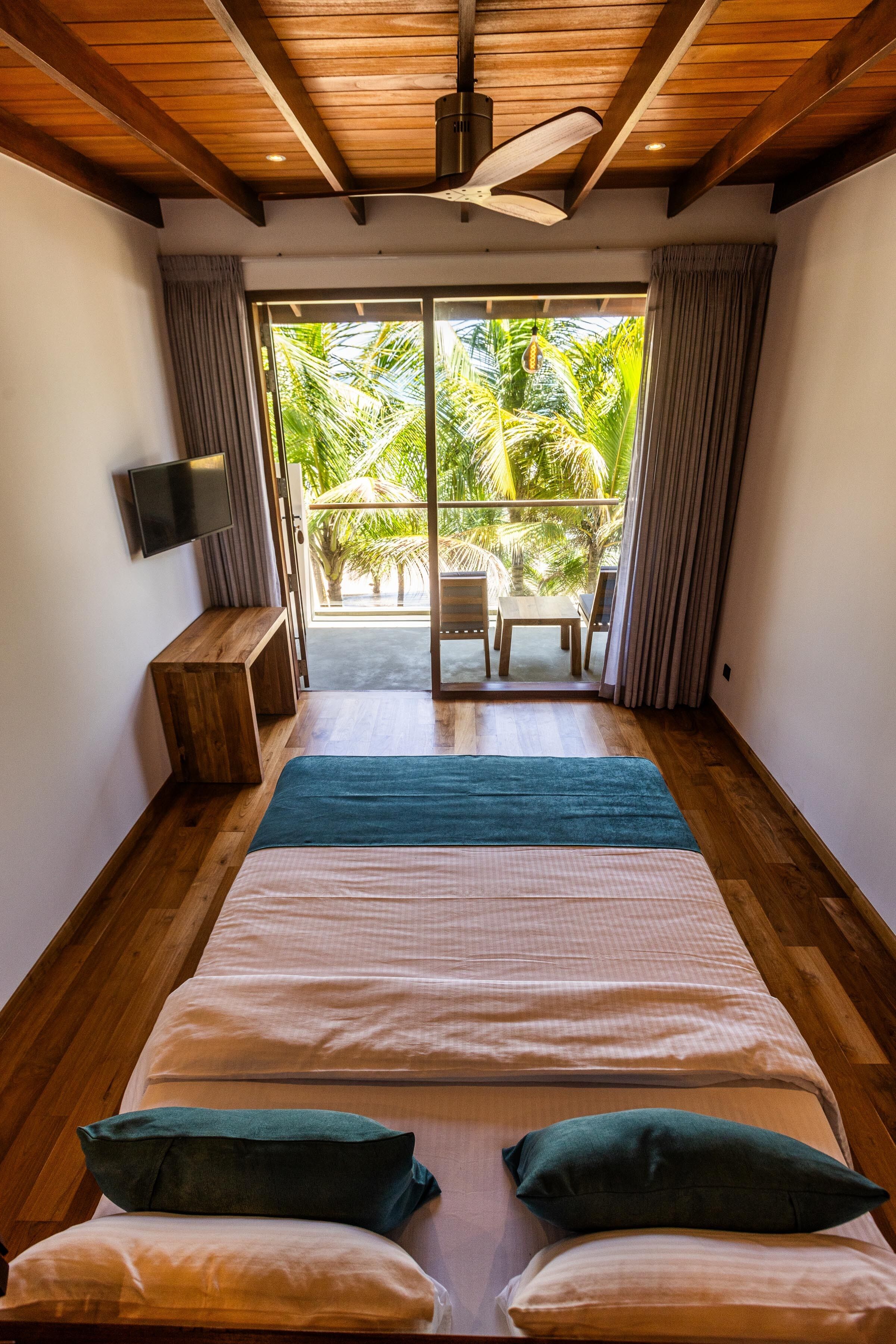A bedroom with a large bed, a TV on the wall, and a view of a balcony with outdoor furniture.